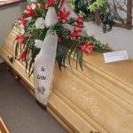 Heller Sarg mit Liliengesteck und Schleife